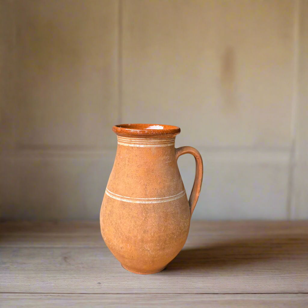 Terracotta pitcher on a wooden surface with a neutral background