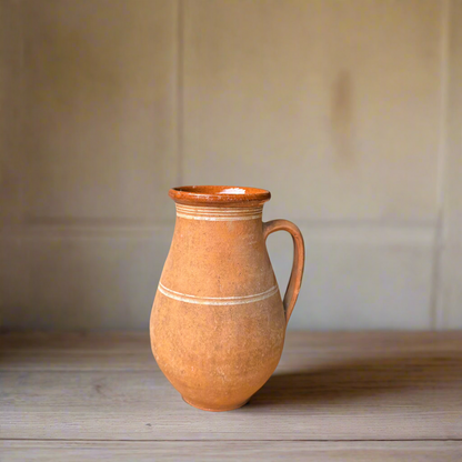 Terracotta pitcher on a wooden surface with a neutral background
